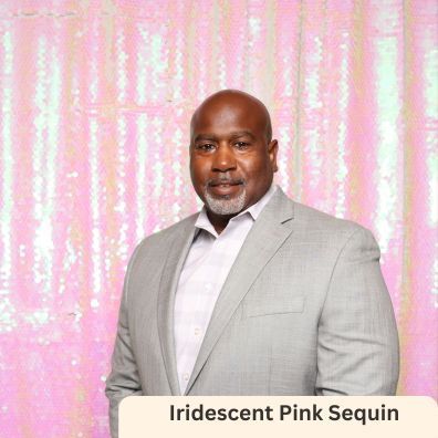 A man in a suit is standing in front of a pink sequin backdrop.