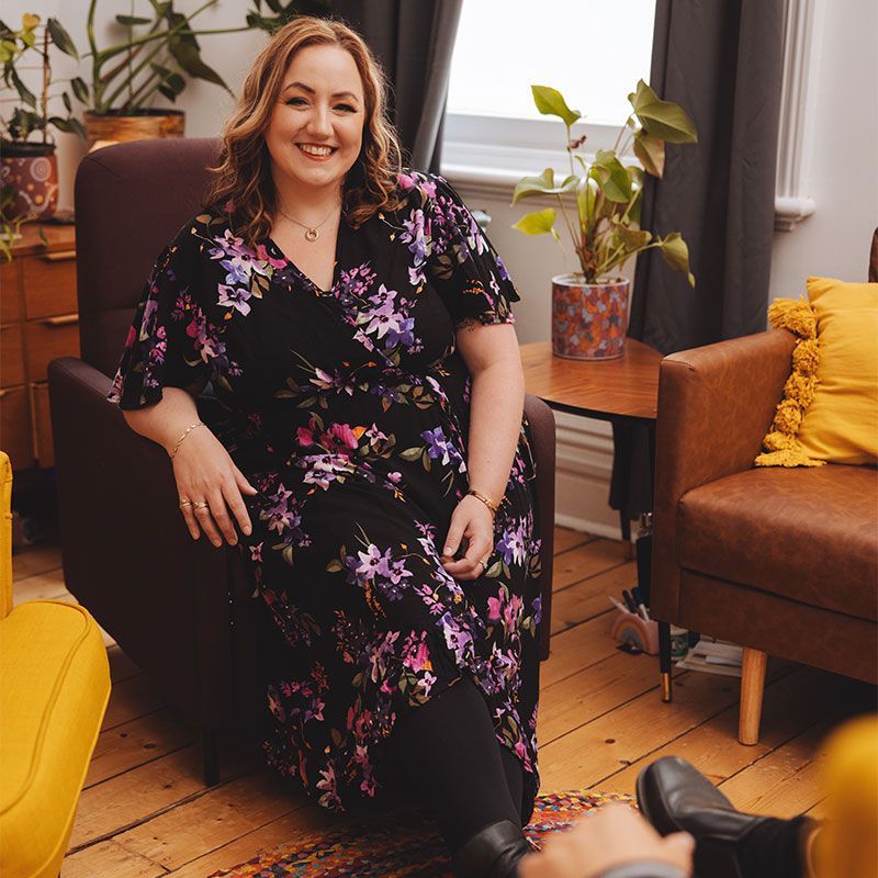 A woman in a floral dress is sitting in a chair in a living room.