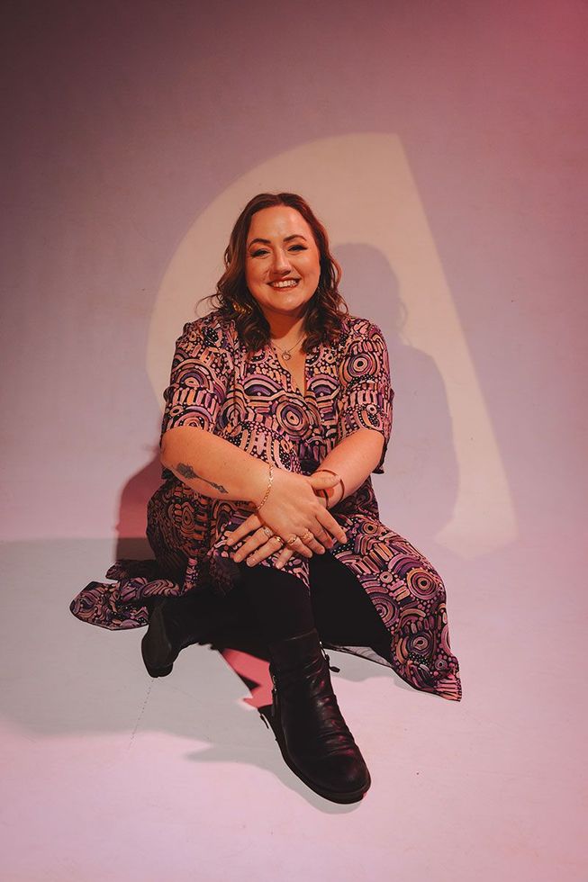A woman in a floral dress is sitting on the floor with her legs crossed.