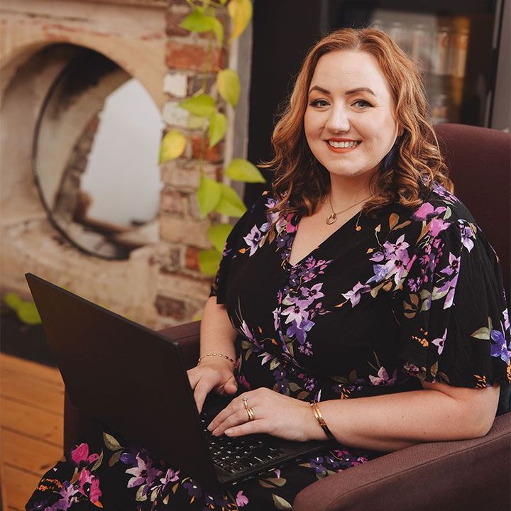 A woman in a purple dress is sitting in a chair in front of a fireplace.