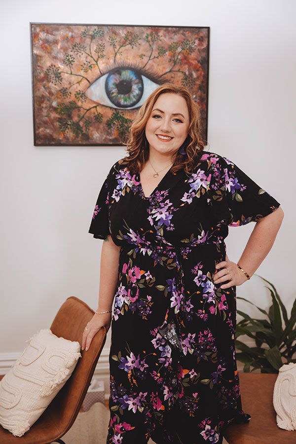 A woman in a floral dress is standing in front of a painting of an eye.
