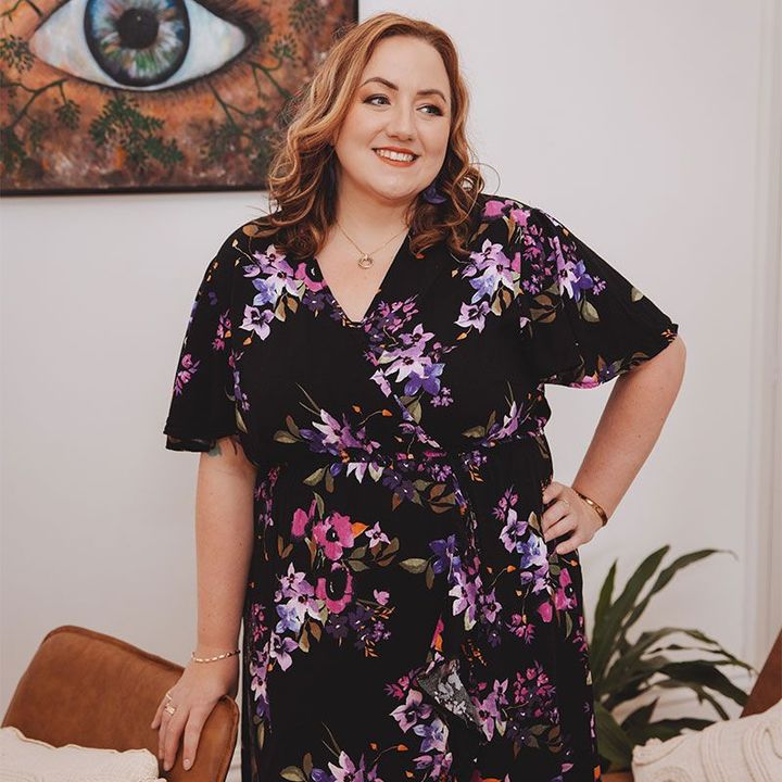 A woman in a floral dress is standing in front of a painting of an eye.