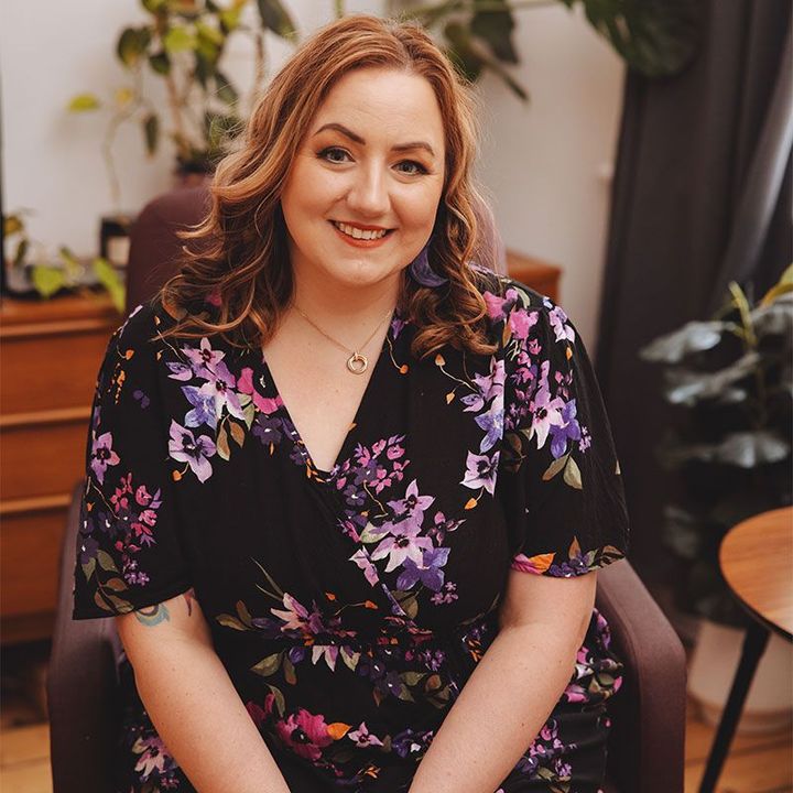 A woman in a floral dress is sitting in a chair.