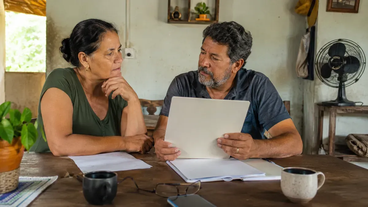 Família rural brasileira em casa simples, organizando documentos e conversando sobre aposentadoria rural. Família rural organiza documentos de segurado especial