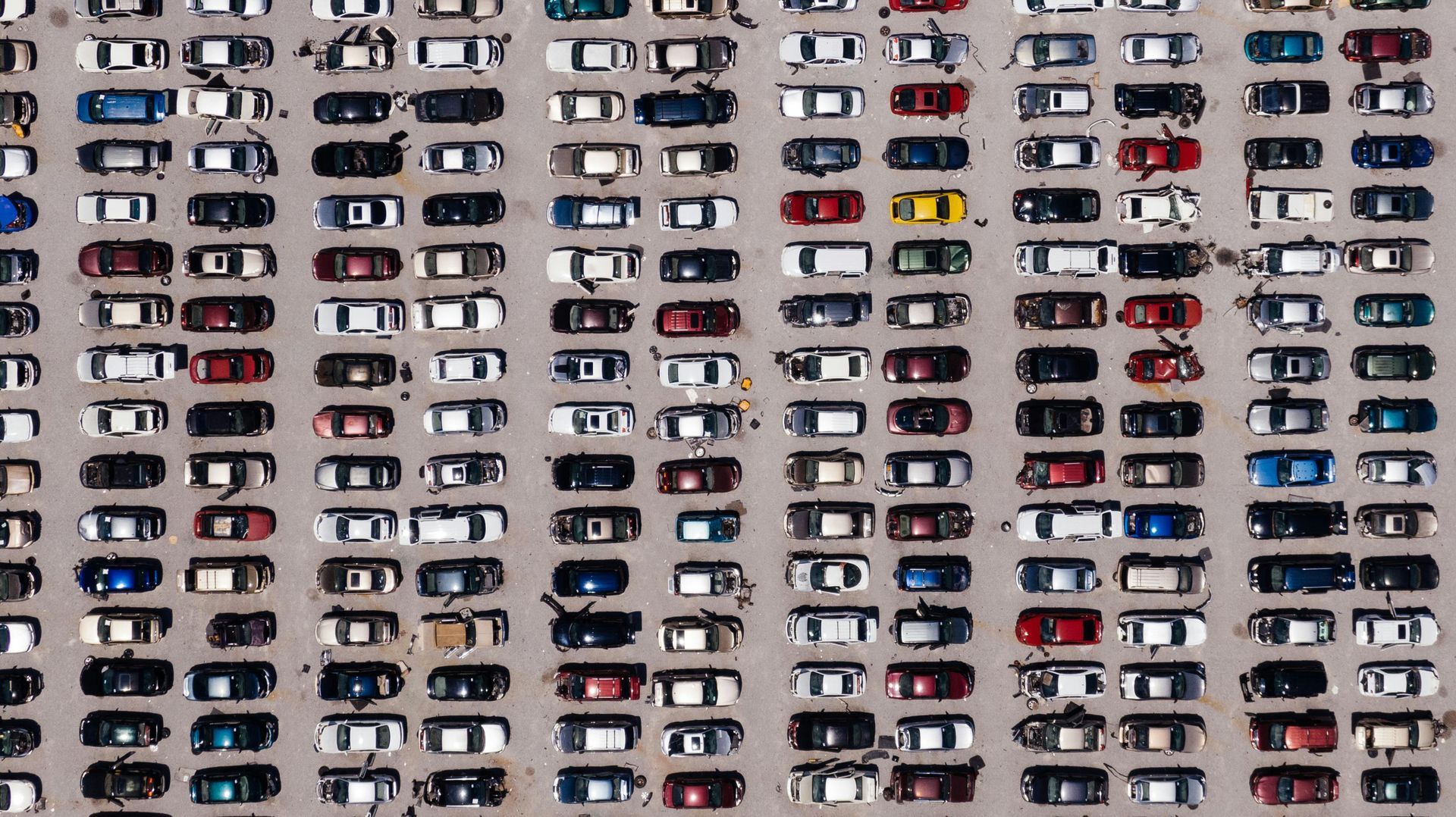 Aerial view of a packed parking lot; cars are mostly white, with some red, blue, and black.