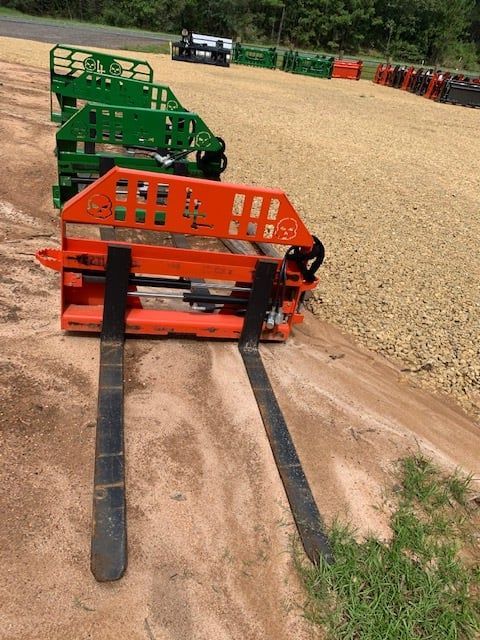 Orange and green forklift attachments parked on gravel.