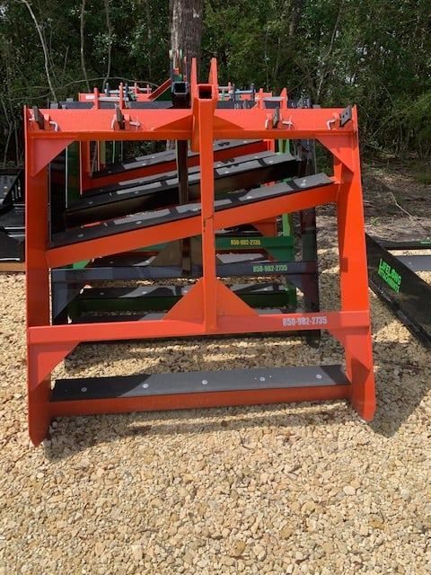 Orange metal hay bale grapple on gravel.