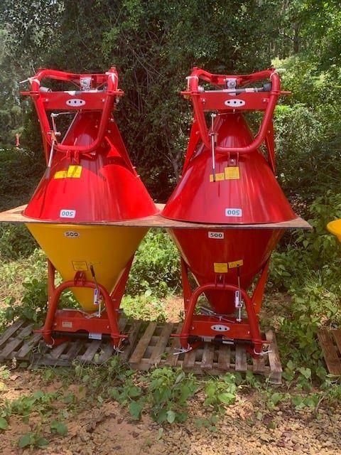 Two red and yellow conical fertilizer spreaders on a wooden pallet, outdoors.