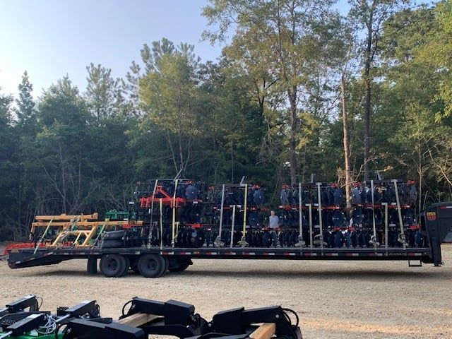 A trailer loaded with numerous black and red tractors in a wooded area.