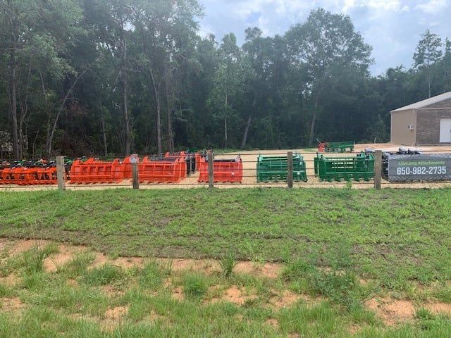 Rows of orange and green metal farm implements in a grassy field with a building and trees in the background.