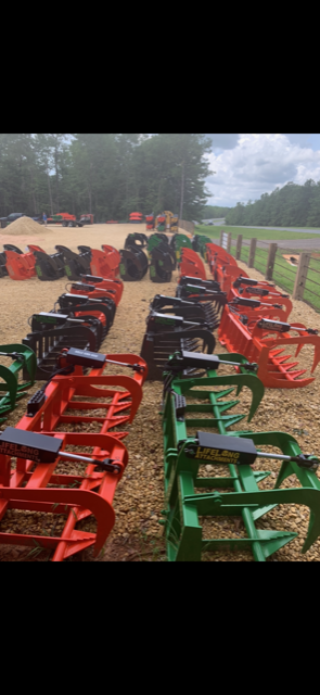 Rows of red, black, and green grapple buckets on a gravel lot, trees in the background.