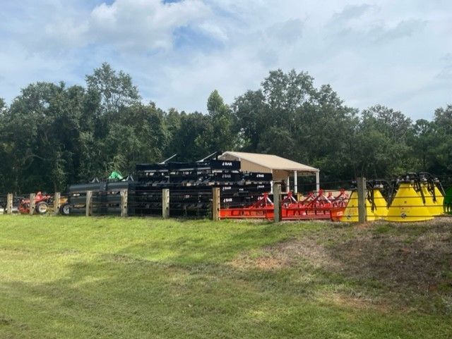 Agricultural equipment display on a grassy field; shed in background under cloudy sky.