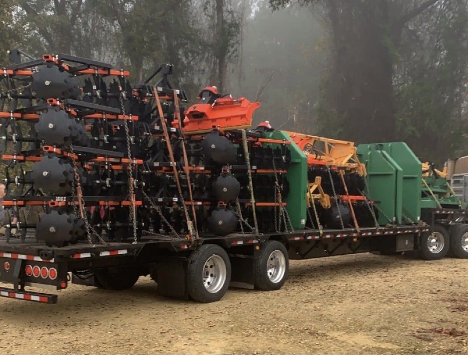 A flatbed truck loaded with agricultural equipment, including tanks, sitting on a dirt road.