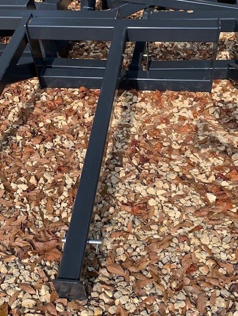 Black metal frame section on a bed of brown and gray gravel and fallen leaves.