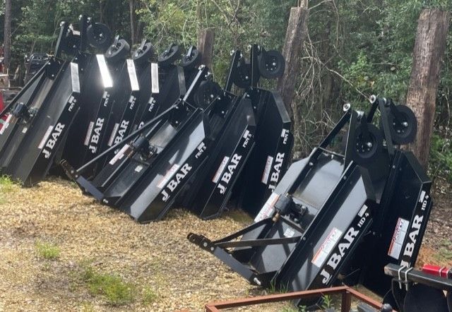 Black J Bar brush cutter implements leaning against a fence outdoors.