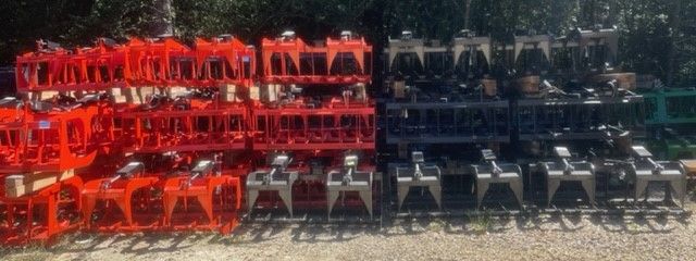 Rows of metal farm equipment in red, gray, black, and green arranged outside.