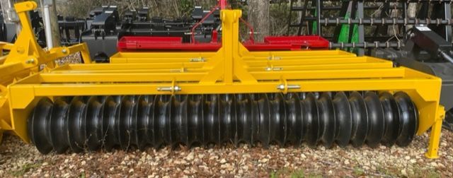 Yellow and black agricultural roller on gravel.
