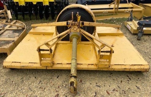 Yellow rotary mower, top view, attached to a tractor's power take-off (PTO), on a gravel lot.