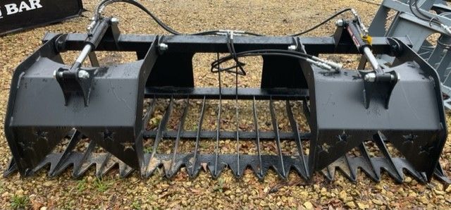 A black grapple attachment for a construction machine. The attachment has sharp teeth and two hydraulic cylinders.