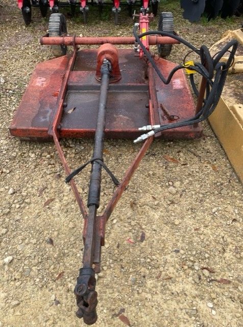 Red rotary cutter implement, attached to a tractor, for cutting grass and weeds.