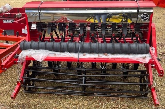 Red agricultural seed drill machine with black components, outdoors.