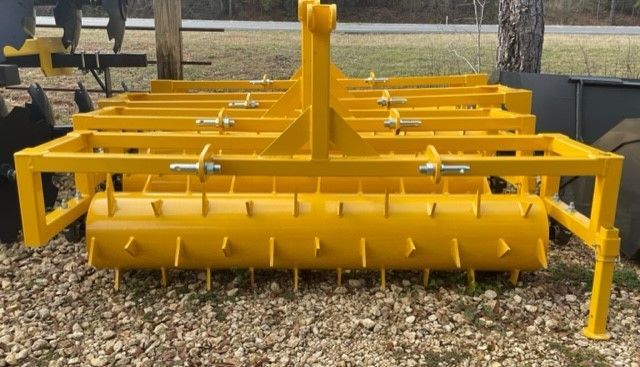 Yellow tractor-pulled pasture aerator with rotating drum and spikes.