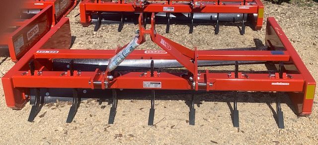 Red tractor box blade with downward facing tines.