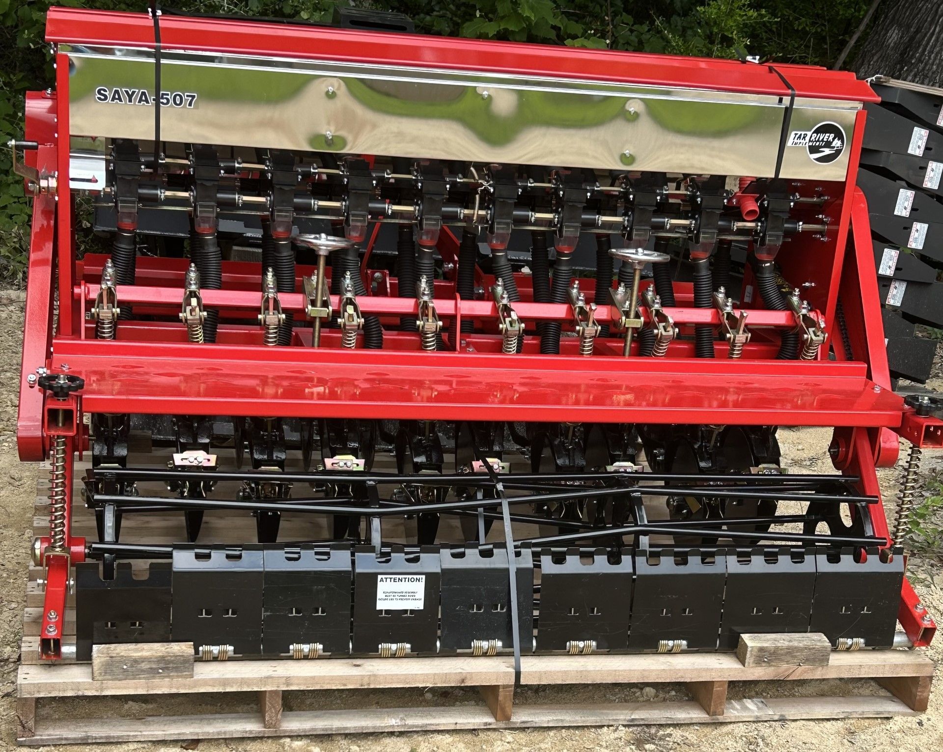 Red agricultural planter with metal seed hopper, black row units, and black soil boxes.