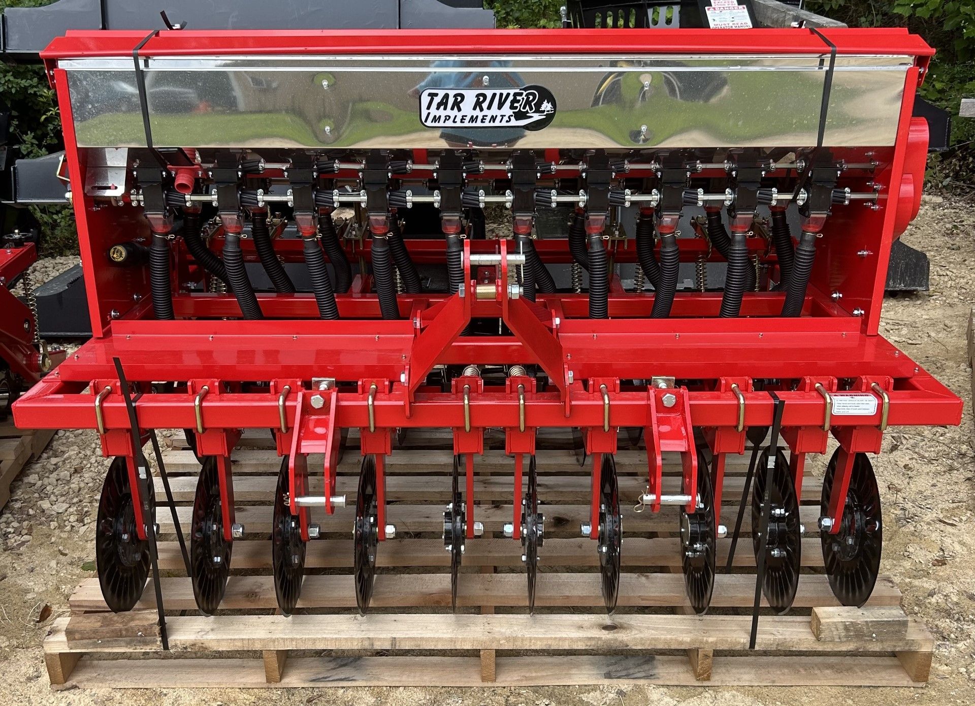 Red Far Rive seeder, attached to a frame, with black wheels. It sits on a wooden pallet.
