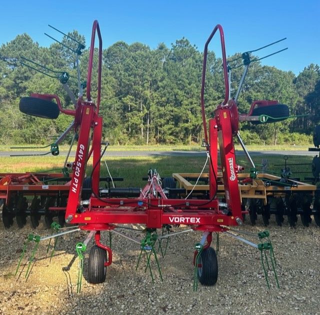 Red agricultural hay rake, Vortex model, with green tines and black tires, in front of trees.