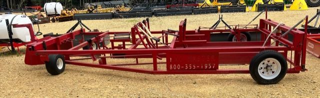 Red, metal agricultural implement with wheels, likely a trailer frame, parked on gravel.