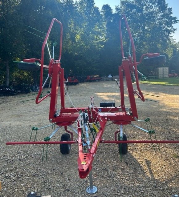 Red agricultural hay rake, outdoors on gravel.