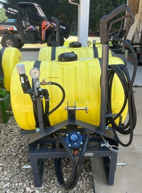 Yellow tank sprayer with black frame, gauge, and hoses, outdoors.