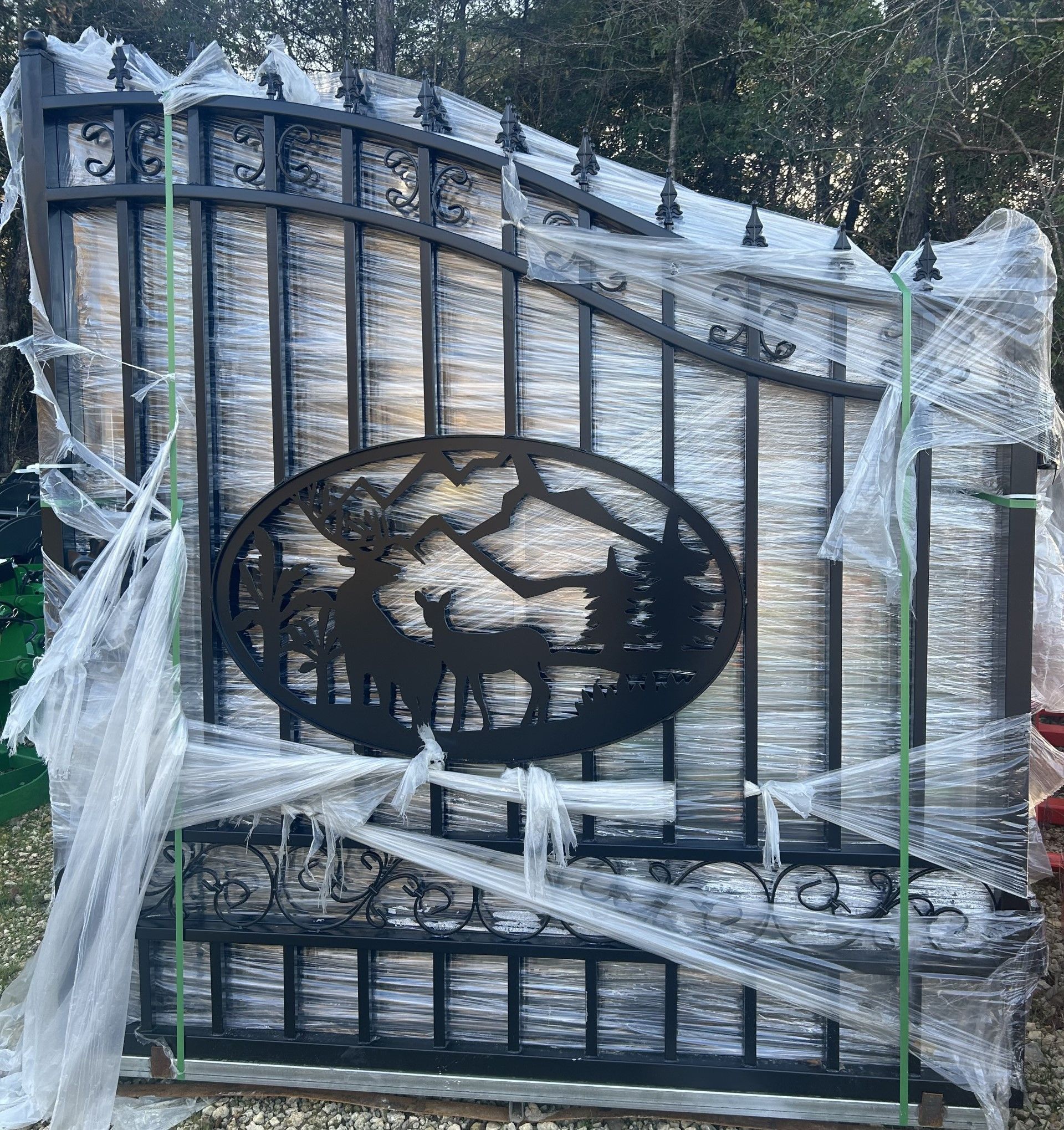 Black metal gate with mountain and deer design, wrapped in plastic.