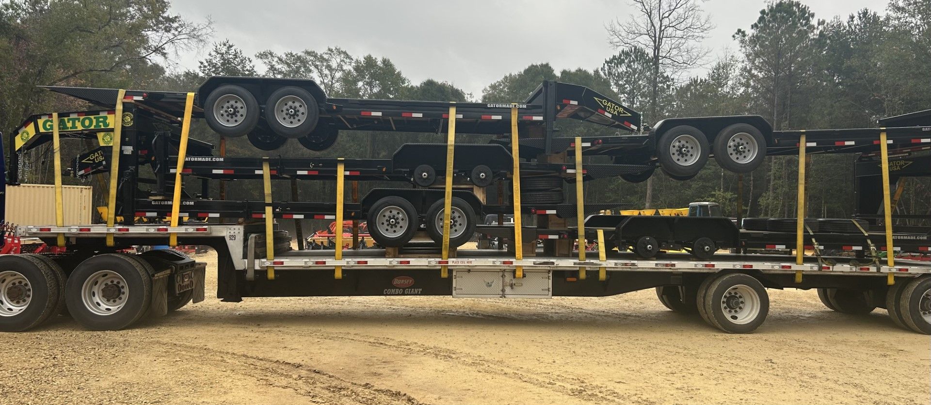 A semi-truck loaded with multiple black trailers, stacked on top of each other, on a dirt road.
