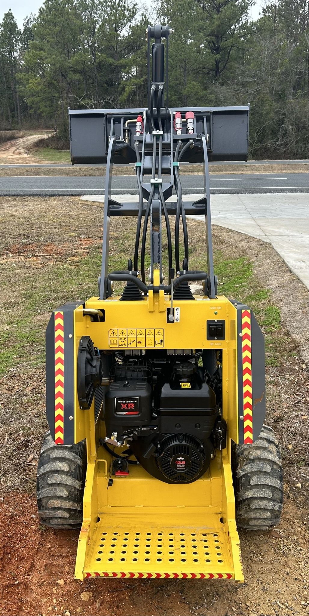 Yellow mini skid steer with raised loader bucket, outdoor setting.