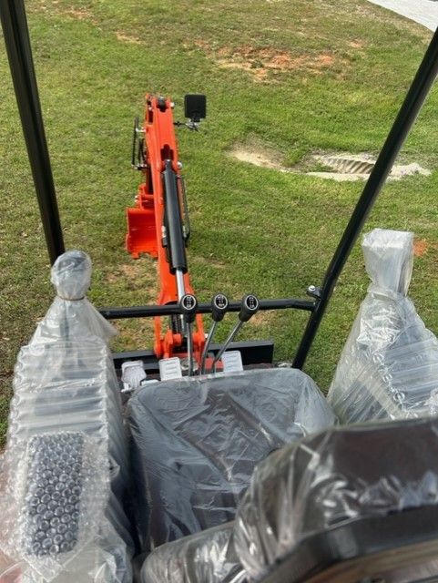 Interior view of a small orange excavator. Operator seat and controls are visible. Safety roll cage.