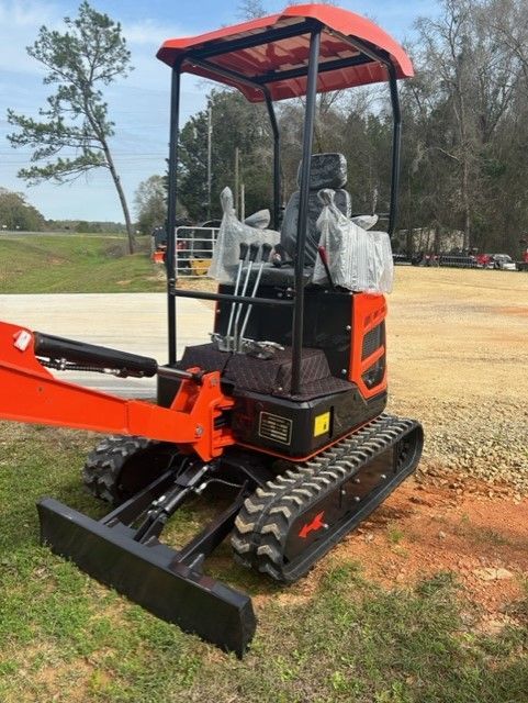 Orange and black mini excavator with canopy, parked on grass.