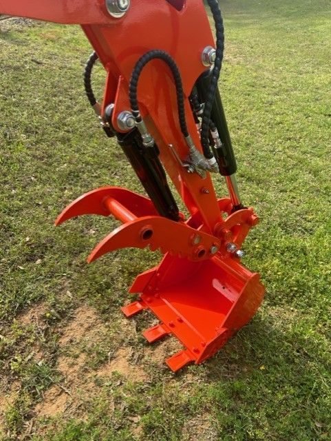 Orange excavator bucket with grapple attachment, outdoors on grass.