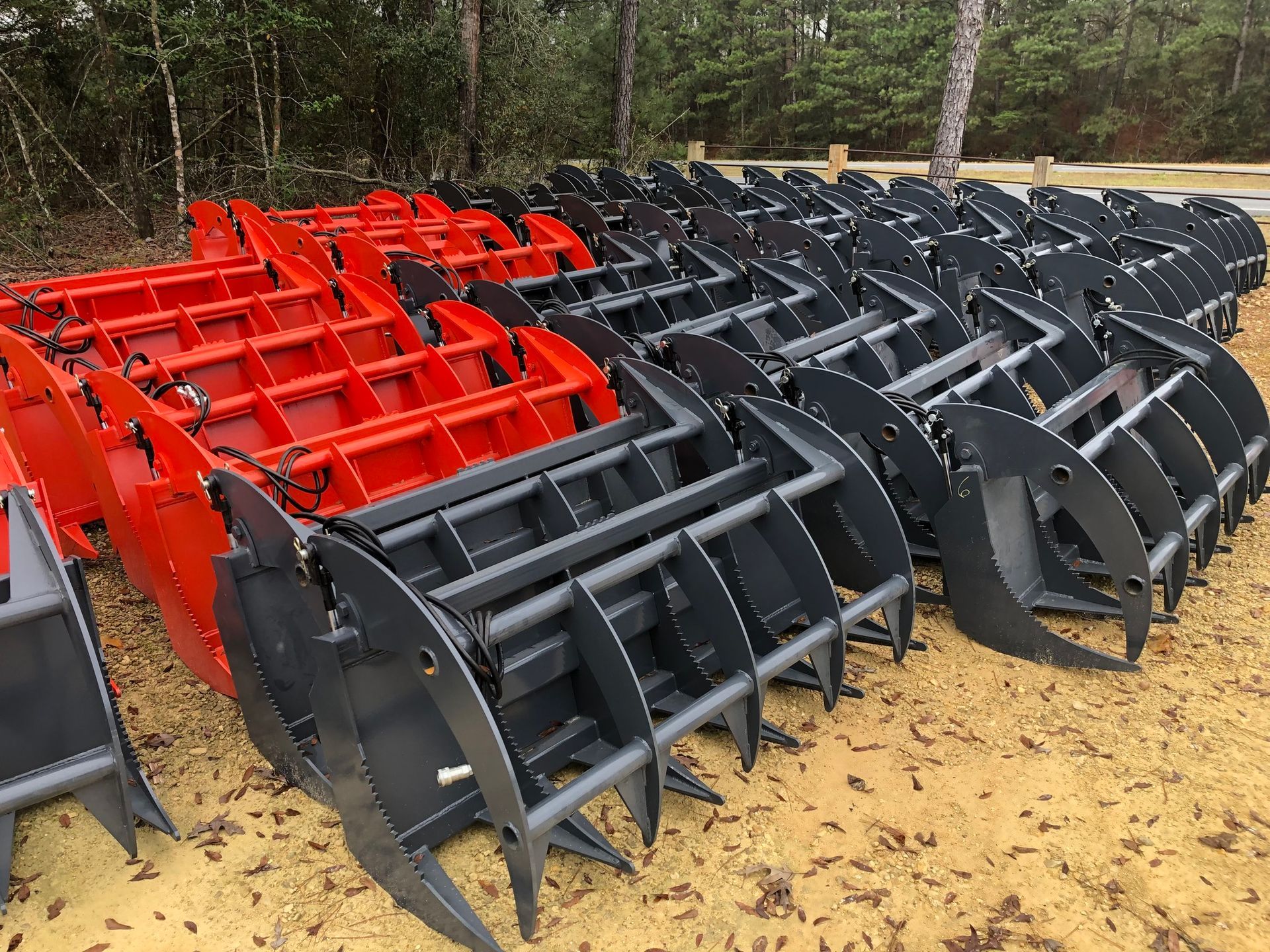 Stacks of red and gray grapple attachments for construction equipment.