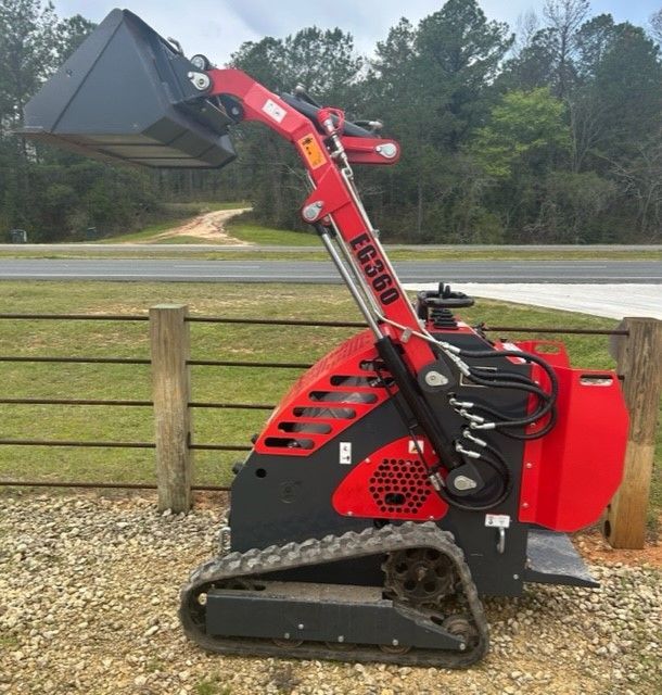 Red and black tracked mini skid steer loader with bucket outdoors. 