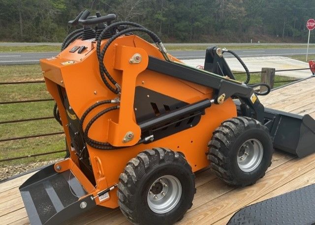Orange mini skid steer loader with bucket attachment on a trailer.