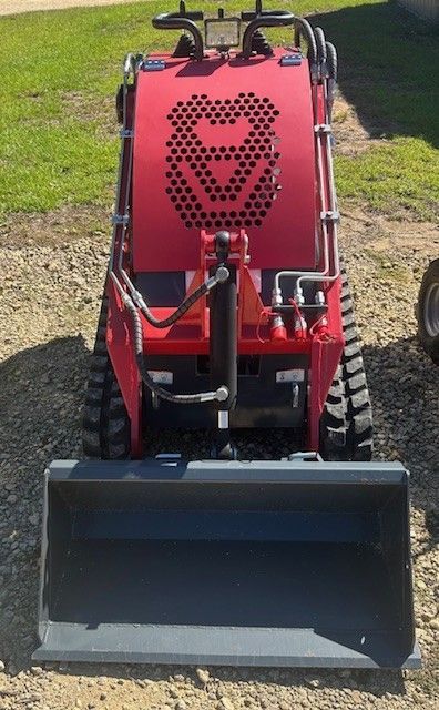Red mini skid steer with bucket attachment, on grass.