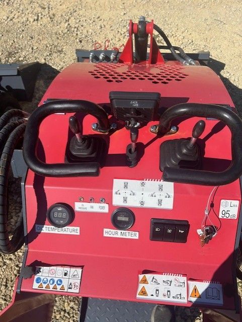 Red machine control panel with joysticks, gauges, and switches for operating machinery.