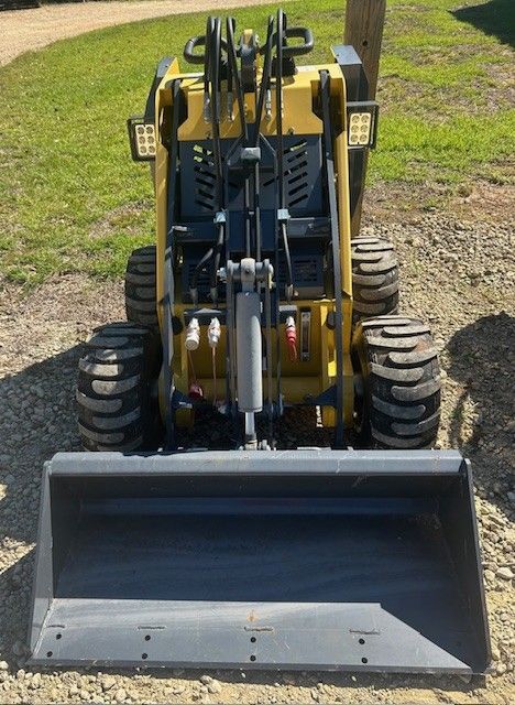 Yellow and gray mini skid steer with a bucket, parked outdoors.