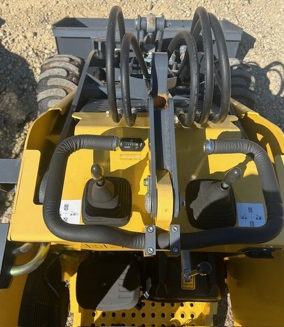 Top-down view of a yellow construction machine's control panel with two handles and a joystick.