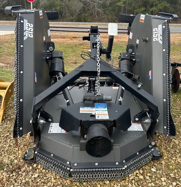 Dark gray brush cutter on a gravel surface. It has safety chains, blades, and is in an outdoor setting.