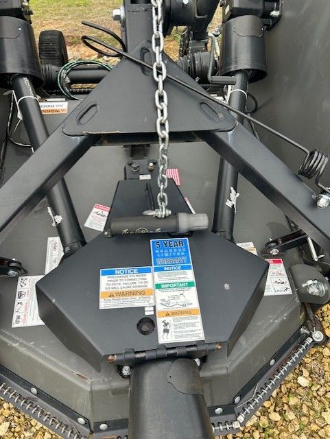Top-down view of a black tractor implement. A chain hangs from the center. Warning labels are visible.