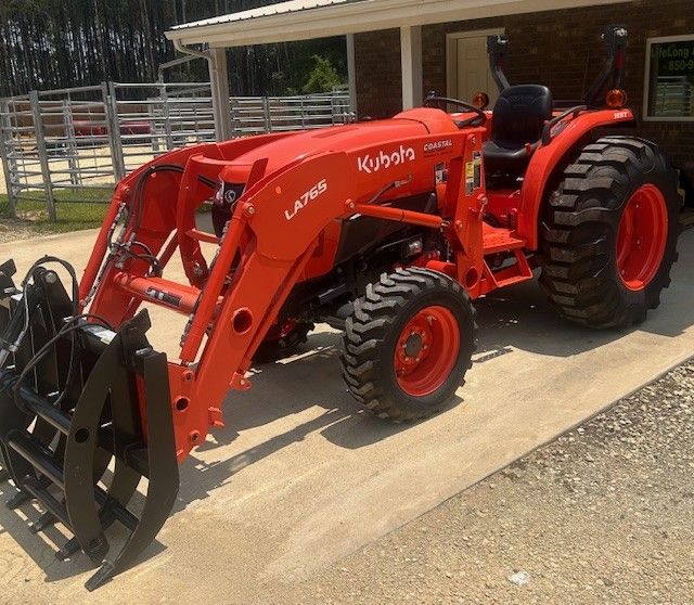 Orange Kubota tractor with front loader, parked on concrete.