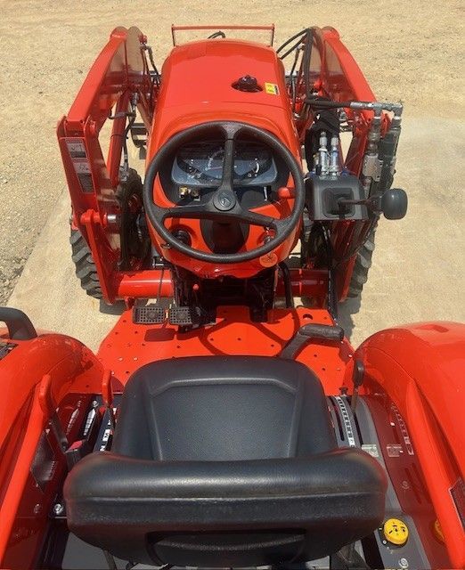 Red tractor, front view, with steering wheel, seat, and loader arms.